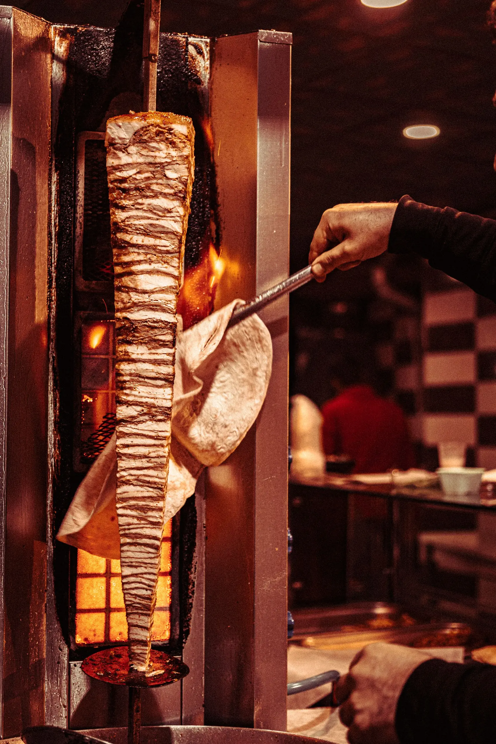 A cook carving shawarma from the spit under a warm hanging lamp