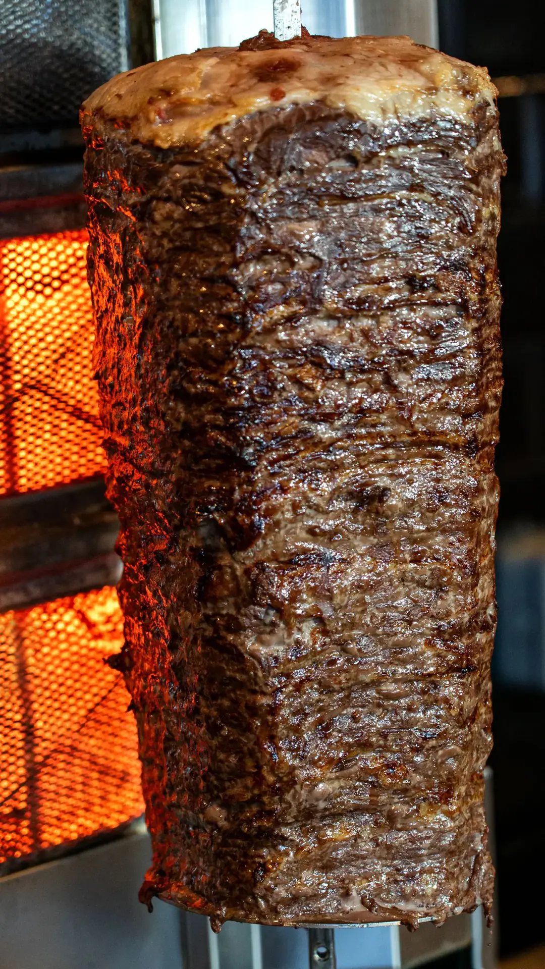 A finished cone of shawarma on the spit, lit by the heater